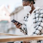 Mulher usando o celular para navegar na internet, próxima a uma bicicleta e a uma grade metálica.