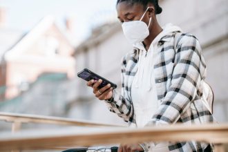 Mulher usando o celular para navegar na internet, próxima a uma bicicleta e a uma grade metálica.