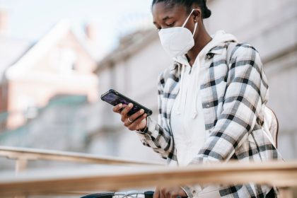 Mulher usando o celular para navegar na internet, próxima a uma bicicleta e a uma grade metálica.