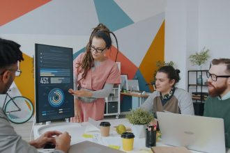 Equipe de profissionais analisa dados exibidos em um monitor durante reunião em escritório.
