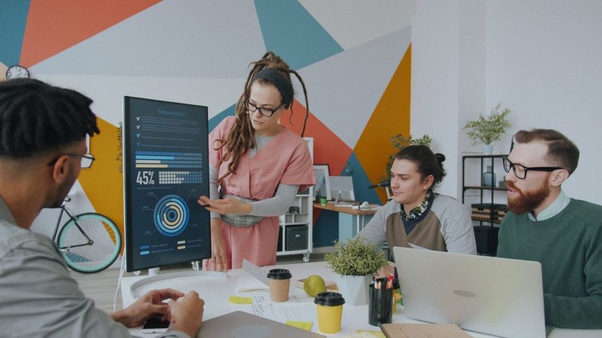 Equipe de profissionais analisa dados exibidos em um monitor durante reunião em escritório.