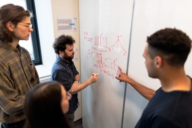 Grupo de engenheiros reúne-se diante de um quadro branco para discutir dados em um ambiente de pesquisa.