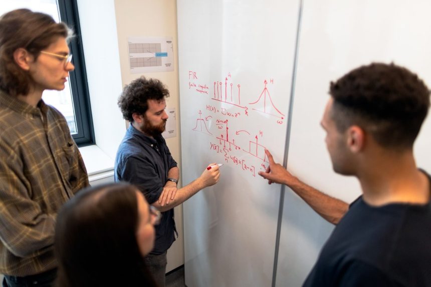 Grupo de engenheiros reúne-se diante de um quadro branco para discutir dados em um ambiente de pesquisa.