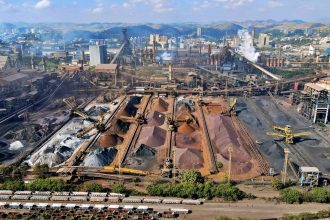 Vista aérea de uma instalação de mineração no Brasil, com máquinas industriais e pilhas de escória.
