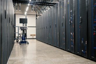 Sala de data center com gabinetes metálicos, servidores, equipamentos de rede e cabos organizados.